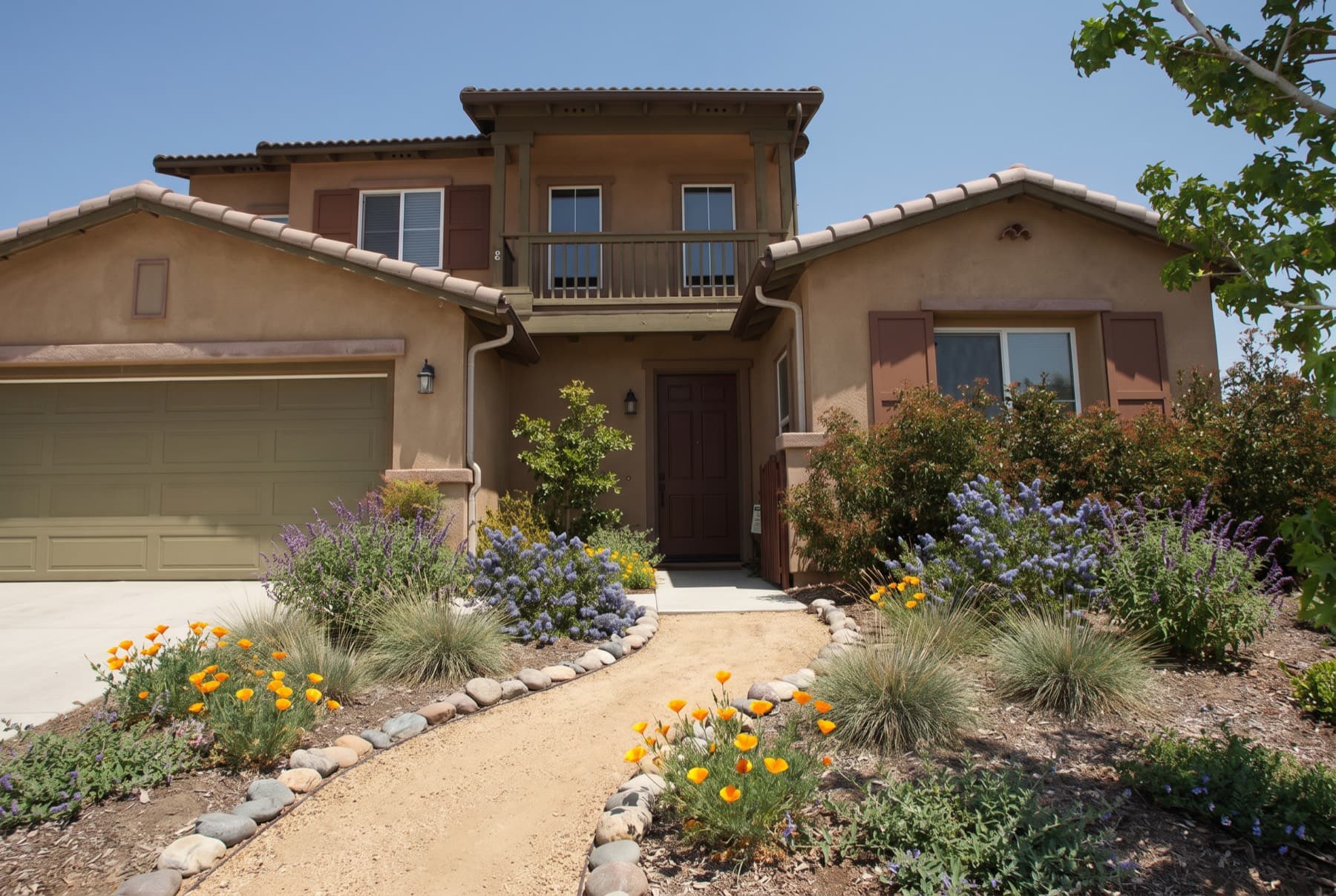 A stucco house with a decomposed granite path edged in river rock, California poppies, ceanothus, sages and blue grasses.